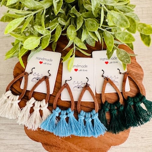 May include: Handmade earrings with wooden teardrop frames and colorful tassels. The earrings are white, light blue, and dark green. Each pair has a tag that says "Handmade with Love".
