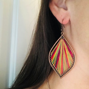 May include: A pair of colourful dangle earrings with a geometric design. The earrings are made of metal and feature a variety of colours, including red, yellow, green, and blue. The earrings are suspended from a small hook.