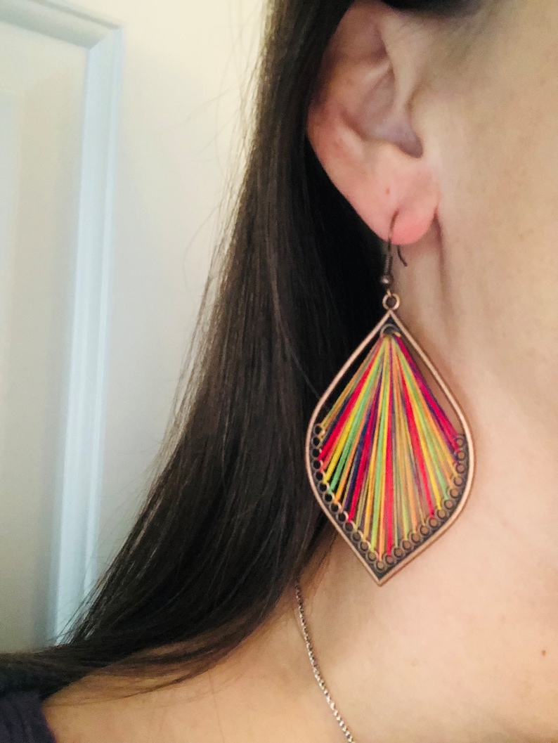 May include: A pair of colourful dangle earrings with a geometric design. The earrings are made of metal and feature a variety of colours, including red, yellow, green, and blue. The earrings are suspended from a small hook.