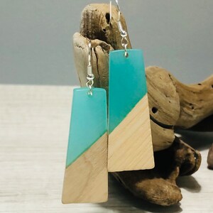 May include: A pair of turquoise and wood earrings. The earrings are rectangular in shape and have a diagonal line of wood across the turquoise resin. The earrings are hanging from silver hooks.