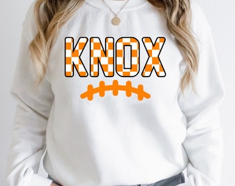 May include: White sweatshirt with an orange and white chequered "KNOX" graphic and a football design.