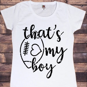 May include: White t-shirt with a black graphic of a football with a heart inside and the text "that's my boy".