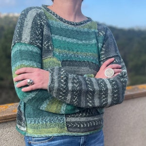 May include: A green and grey striped sweater with a patchwork design. The sweater has a crew neck and long sleeves.