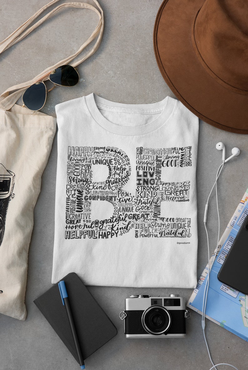 Puede incluir: Una camiseta blanca con un dise&ntilde;o gr&aacute;fico negro en forma de la letra "R" compuesta por palabras como "feliz", "fuerte", "genial", "amor", "amable", "&uacute;nico", "servicial" y "agradecido".