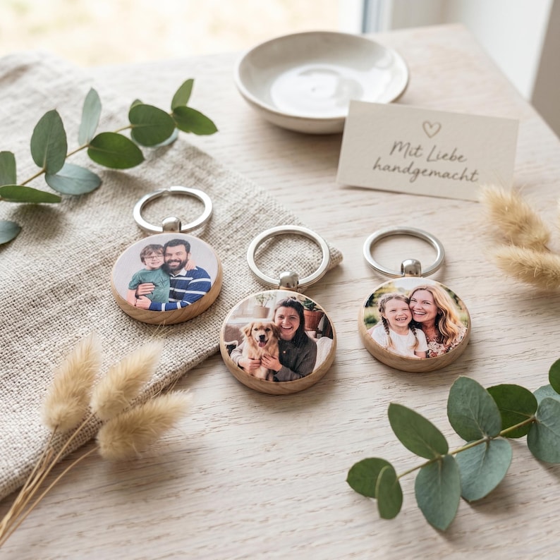 K&ouml;nnte beinhalten: Drei Holz-Schl&uuml;sselanh&auml;nger mit silbernen Ringen, jeweils mit einem anderen Familienfoto. Die Schl&uuml;sselanh&auml;nger sind rund und haben eine nat&uuml;rliche Holzmaserung. Eine kleine Karte mit handgeschriebenem Text und einem Herz ist zu sehen.