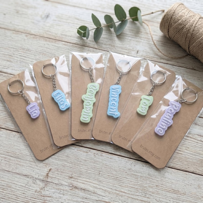 K&ouml;nnte beinhalten: Schl&uuml;sselanh&auml;nger in Pastellfarben mit den Namen "Lia", "Elias", "Benjamin", "Vincent", "Tom" und "Pauline". Jeder Anh&auml;nger ist auf einer braunen Karte mit dem Text "brutec.etsy.com" verpackt.