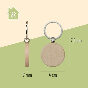 K&ouml;nnte beinhalten: Ein Holzschl&uuml;sselanh&auml;nger mit einem silbernen Ring. Der runde Holzanh&auml;nger hat einen Durchmesser von 4 cm und ist 7 mm dick. Der Schl&uuml;sselanh&auml;nger ist 7,5 cm lang. Der Hintergrund ist hellgr&uuml;n und beige.