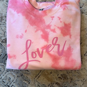 May include: Pink tie-dye sweatshirt with the word "lover" written in pink on the front.