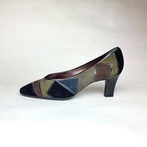 May include: A pair of black suede pumps with a geometric patchwork design in shades of green, brown, and blue. The shoes have a pointed toe and a medium-height heel.