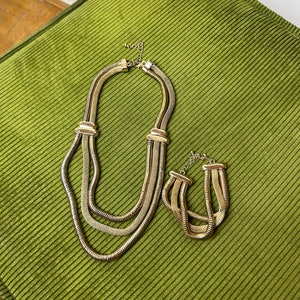 May include: A gold-toned necklace and bracelet set with a layered chain design. The necklace is longer and has three strands of chain, while the bracelet has two strands.