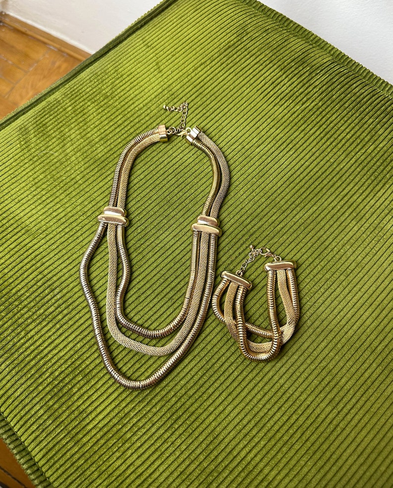 May include: A gold-toned necklace and bracelet set with a layered chain design. The necklace is longer and has three strands of chain, while the bracelet has two strands.