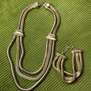 May include: A gold-tone layered chain necklace and bracelet set. The necklace has three strands of chain, and the bracelet has two strands.