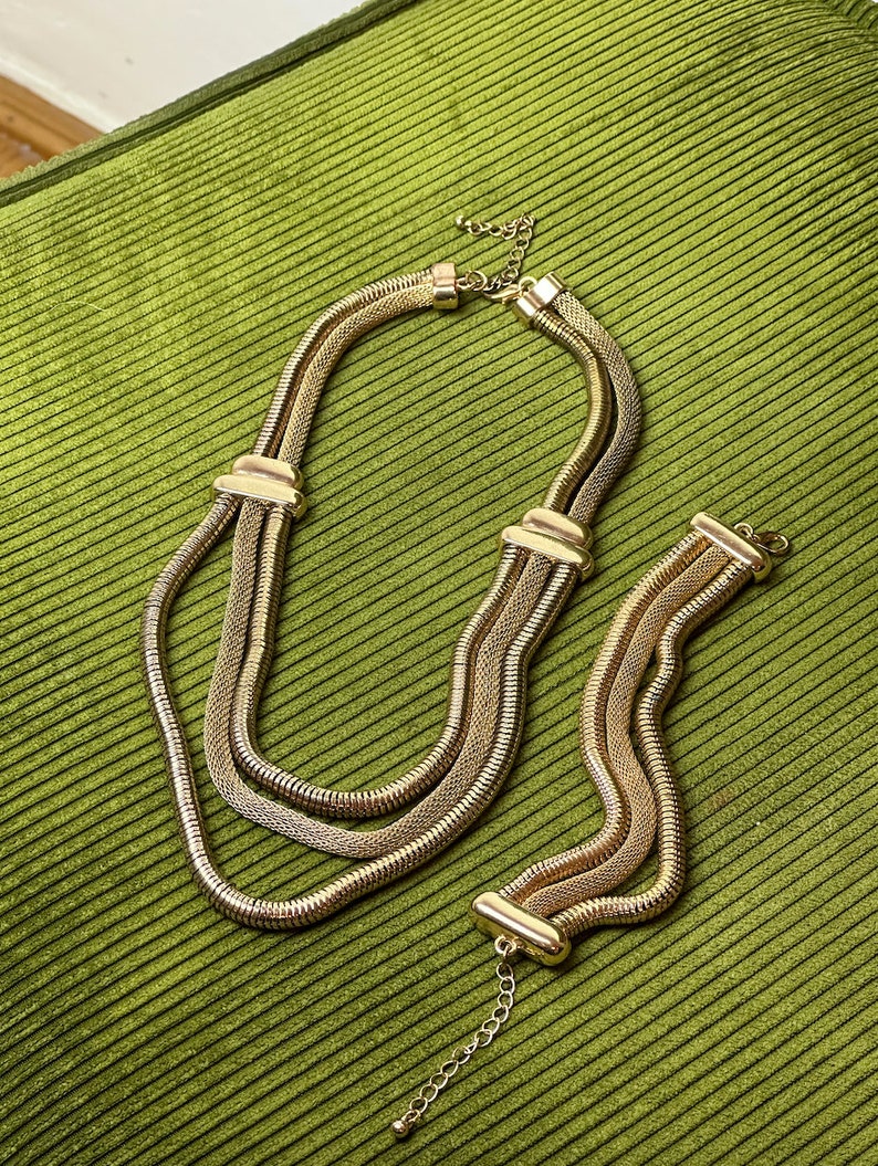May include: A gold-toned necklace and bracelet set with a chain link design. The necklace is layered with three strands of chain.