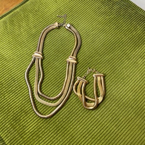 May include: A gold-tone layered necklace and matching bracelet set. The necklace has three strands of chain and the bracelet has two strands.