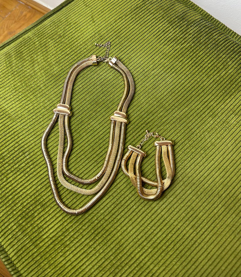 May include: A gold-tone layered necklace and matching bracelet set. The necklace has three strands of chain and the bracelet has two strands.