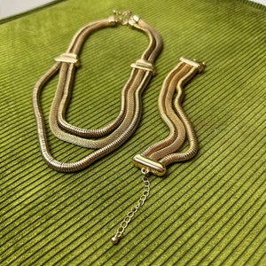 May include: A gold-toned layered chain necklace and bracelet set. The necklace and bracelet are made of multiple strands of linked chain.