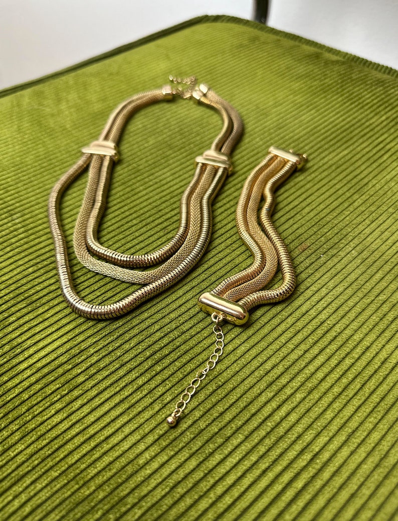 May include: A gold-toned layered chain necklace and bracelet set. The necklace and bracelet are made of multiple strands of linked chain.