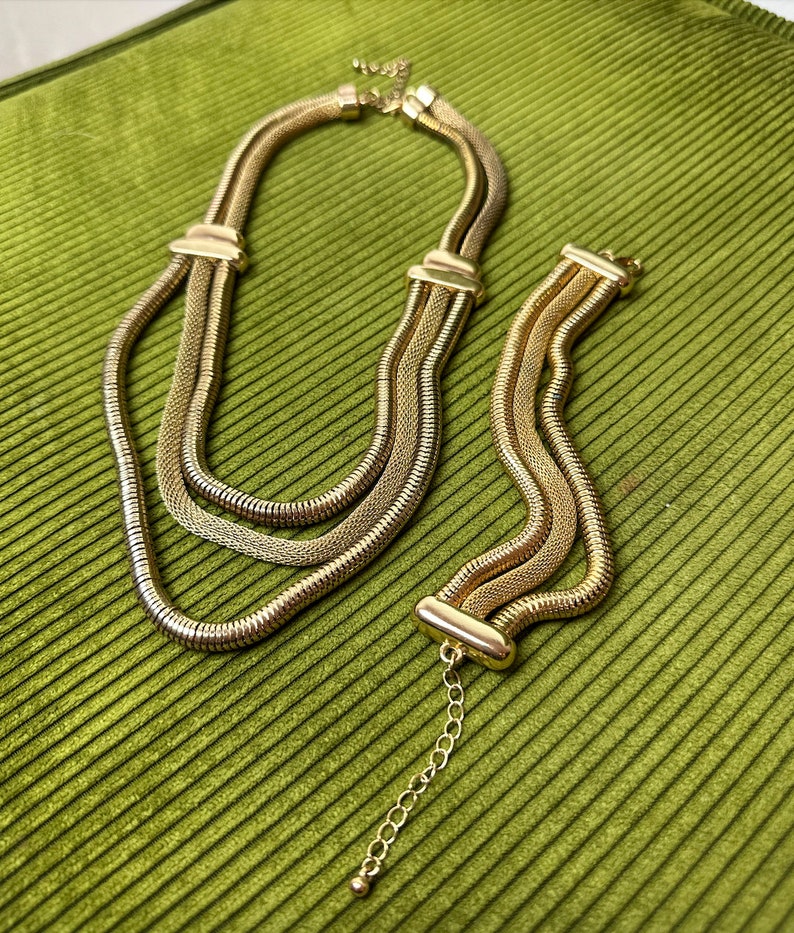May include: A gold-toned necklace and bracelet set with a chain link design. The necklace is layered with three strands of chain.
