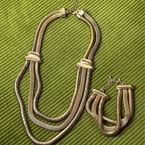 May include: A gold-toned necklace and bracelet set with a chain link design. The necklace is layered with three strands of chain.