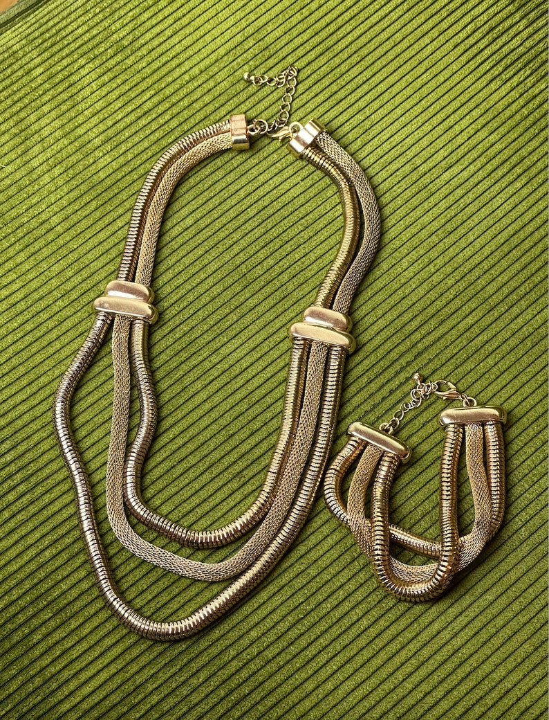 May include: A gold-toned necklace and bracelet set with a chain link design. The necklace is layered with three strands of chain.