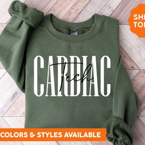 May include: Military green sweatshirt with the text "CARDIAC Tech" in white block letters and a cursive font. The sweatshirt has long sleeves and a crew neck. The words "MORE COLORS & STYLES AVAILABLE" are at the bottom.