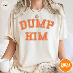 Pu&ograve; includere: Una t-shirt a maniche corte color avorio con la scritta DUMP HIM in un carattere universitario arancione dall'aspetto usurato sul petto. Il capo presenta un girocollo e una vestibilit&agrave; rilassata con lettere dal design semplice e vissuto.
