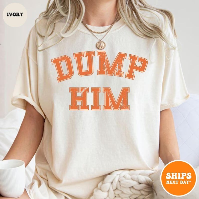 Pu&ograve; includere: Una t-shirt a maniche corte color avorio con la scritta DUMP HIM in un carattere universitario arancione dall'aspetto usurato sul petto. Il capo presenta un girocollo e una vestibilit&agrave; rilassata con lettere dal design semplice e vissuto.