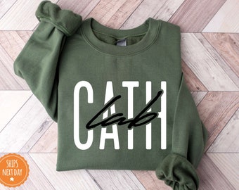 May include: A green sweatshirt with the word "CATH" printed in white letters with a black line through the letters.