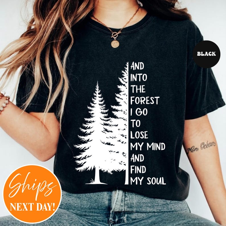 May include: A black short-sleeved t-shirt featuring a white graphic of two pine trees next to the text, AND INTO THE FOREST I GO TO LOSE MY MIND AND FIND MY SOUL. The shirt has a crew neckline and is made of a solid black fabric with a white print.