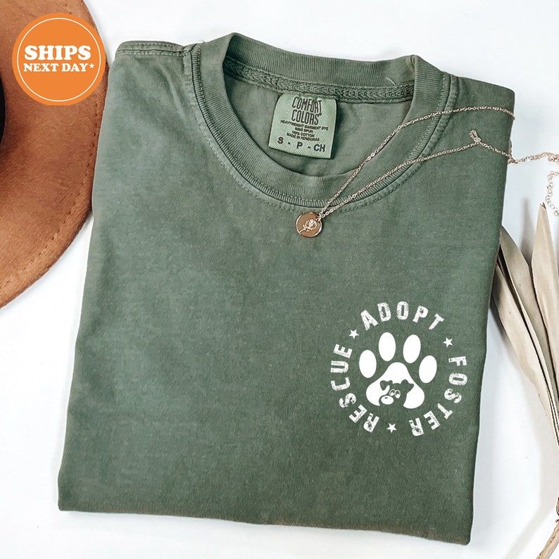 May include: A green t-shirt with a white paw print design that says "Rescue Adopt Foster" in a circle around the paw print.