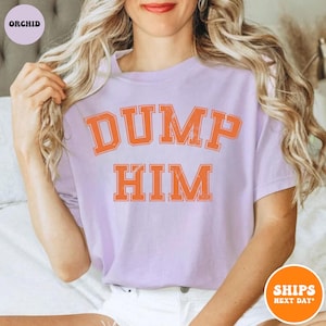 Pu&ograve; includere: Una t-shirt a maniche corte color viola chiaro con la scritta DUMP HIM in un carattere arancione invecchiato in stile college sul petto. La maglia presenta un girocollo e una vestibilit&agrave; rilassata, con la parola ORCHID in un piccolo cerchio.