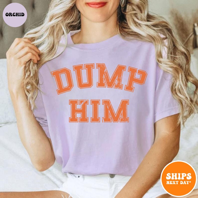 Pu&ograve; includere: Una t-shirt a maniche corte color viola chiaro con la scritta DUMP HIM in un carattere arancione invecchiato in stile college sul petto. La maglia presenta un girocollo e una vestibilit&agrave; rilassata, con la parola ORCHID in un piccolo cerchio.