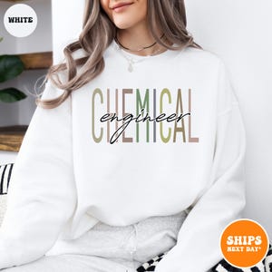 May include: White crewneck sweatshirt with the words "CHEMICAL engineer" printed across the front in a mix of colors. The word "engineer" is in a cursive font. The sweatshirt is a casual style.
