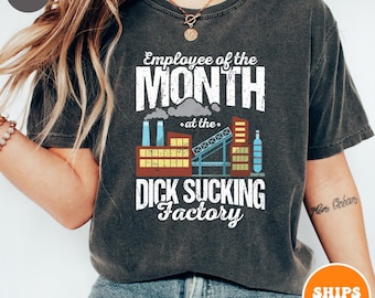 May include: A dark gray t-shirt with a distressed look featuring the text "Employee of the Month at the Dick Sucking Factory". The text is in white with a black outline. The graphic includes a cartoon factory with smoke stacks and a crane.