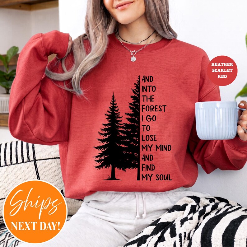May include: A heather scarlet red crewneck sweatshirt featuring a black graphic of two pine trees and the text AND INTO THE FOREST I GO TO LOSE MY MIND AND FIND MY SOUL. The long-sleeved pullover has a ribbed neckline, cuffs, and hem.