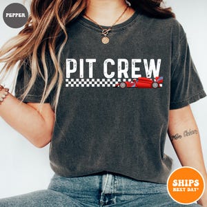May include: A gray t-shirt with the text "PIT CREW" in white with a checkered flag design and a red race car graphic.