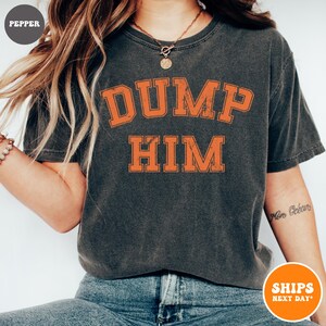 Pu&ograve; includere: Una t-shirt a maniche corte grigio antracite con una stampa grafica arancione in stile college dall'aspetto vissuto sul petto che recita DUMP HIM in grassetto. La maglia presenta un girocollo e un tessuto dall'effetto lavato vintage.