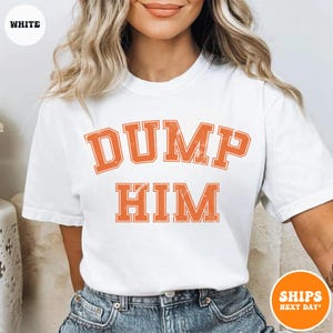 Pu&ograve; includere: Una t-shirt bianca a maniche corte con la scritta DUMP HIM in un carattere arancione invecchiato in stile college sul petto. Il capo presenta un girocollo ed &egrave; abbinato a un paio di jeans blu, offrendo un look casual e semplice.