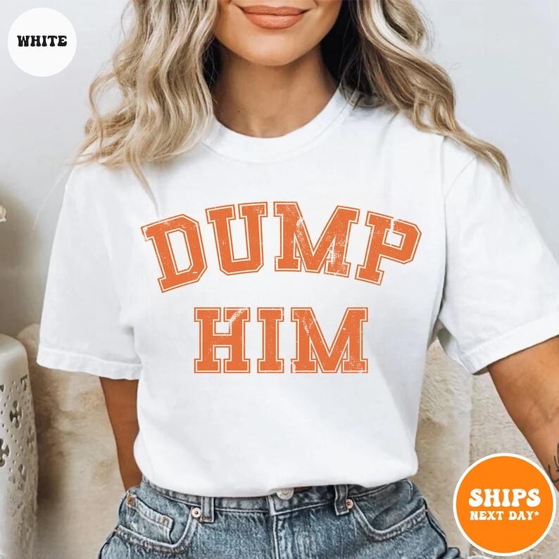 Pu&ograve; includere: Una t-shirt bianca a maniche corte con la scritta DUMP HIM in un carattere arancione invecchiato in stile college sul petto. Il capo presenta un girocollo ed &egrave; abbinato a un paio di jeans blu, offrendo un look casual e semplice.