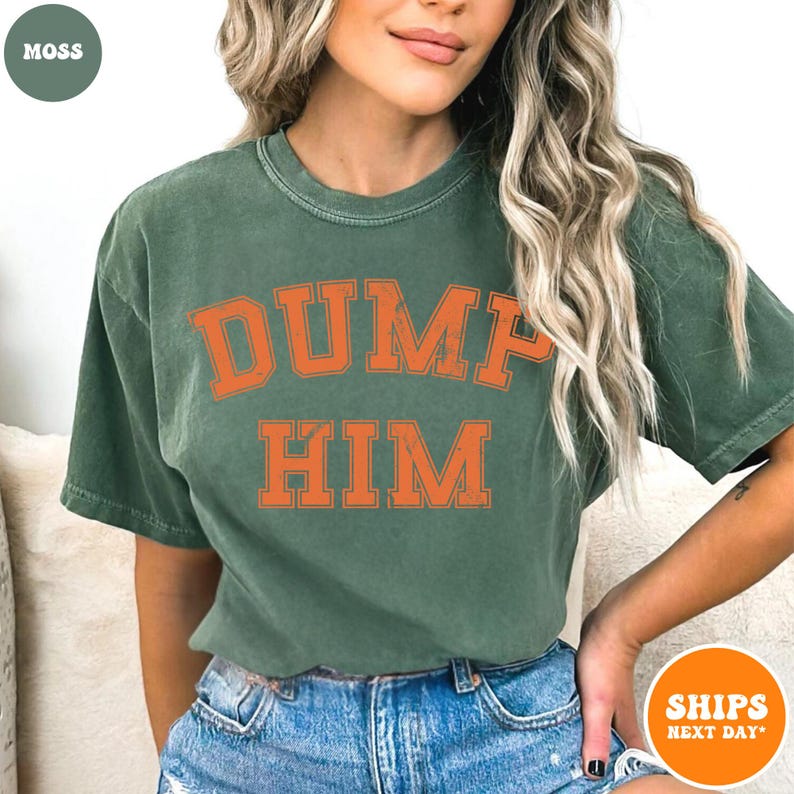 Pu&ograve; includere: Una t-shirt a maniche corte con girocollo color verde muschio, caratterizzata da una stampa grafica arancione dall'effetto vissuto sul petto con la scritta DUMP HIM in un audace carattere universitario arcuato. Il capo ha una texture slavata.