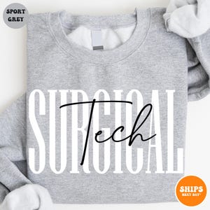 May include: A gray sweatshirt with the text "SURGICAL Tech" printed in white with black lettering. The text is in a bold, stylized font.