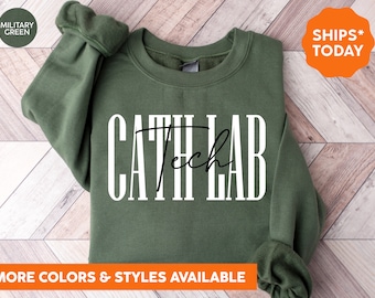 May include: Military green sweatshirt with the text "CATH LAB Tech" in white and black. The sweatshirt has long sleeves and a crew neck. The image also includes the text "MORE COLORS & STYLES AVAILABLE".