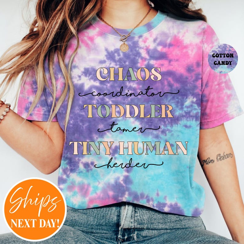 May include: A short-sleeve t-shirt with a pink, purple, and blue tie-dye pattern. The front features the text: CHAOS coordinator, TODDLER tamer, TINY HUMAN herder. A small circular badge in the top right corner reads COTTON CANDY.