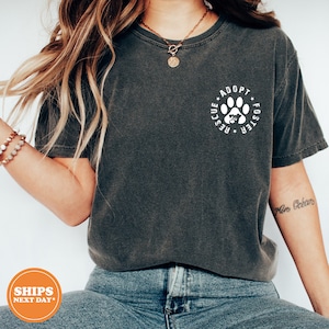 May include: A dark gray t-shirt with a white paw print graphic that says "Adopt, Foster, Rescue" in a circle around the paw print.
