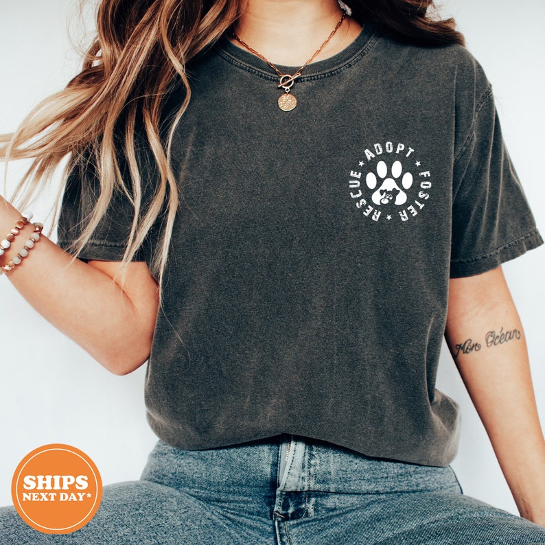 May include: A dark gray t-shirt with a white paw print graphic that says "Adopt, Foster, Rescue" in a circle around the paw print.