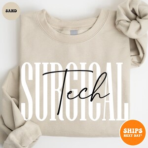 May include: A sand-colored sweatshirt with the text "SURGICAL Tech" printed in white with black lettering.