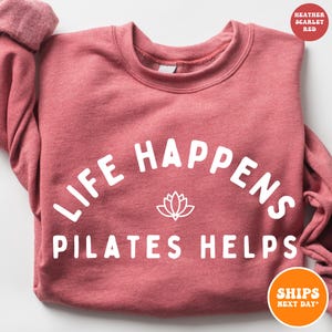 May include: Heather scarlet red sweatshirt with the text "Life Happens Pilates Helps" in white, with a white lotus flower graphic.