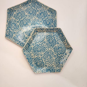 May include: Two hexagonal ceramic trays with a blue and white lace pattern. The smaller tray is stacked on top of the larger tray.