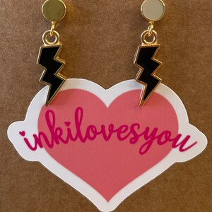 May include: A pair of gold earrings with black lightning bolt charms. The earrings have a simple, minimalist design and are perfect for adding a touch of edgy style to any outfit.