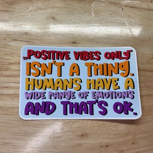 May include: A sticker with a blue background and white border. The text on the sticker reads "POSITIVE VIBES ONLY ISN'T A THING. HUMANS HAVE A WIDE RANGE OF EMOTIONS AND THAT'S OK."
